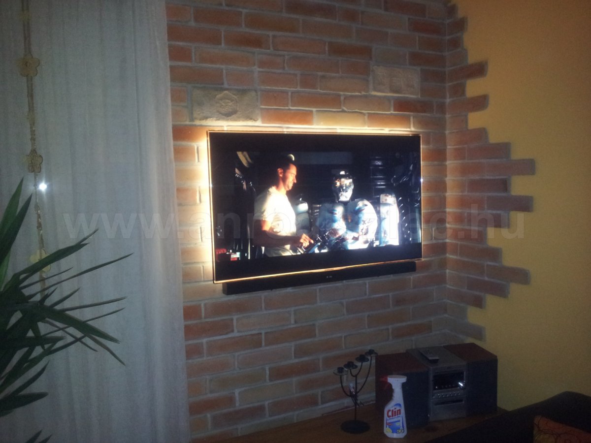 Melegfehér fényű háttérvilágítás téglafalra szerelt tévén.