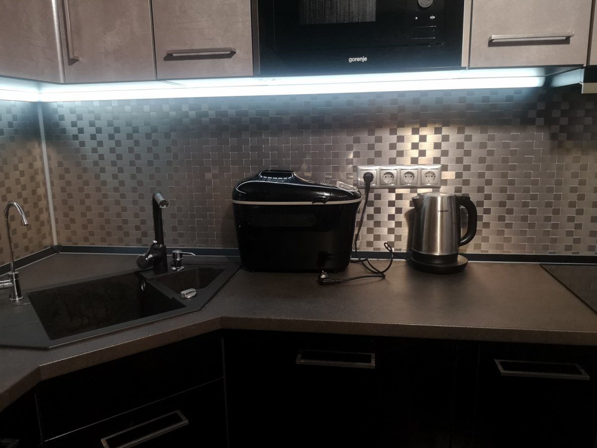 Modern színek egy új konyhában: szürke kapcsolóaljzatok, szürke bútorfront, inox vízforraló, fekete gránit mosogató - praktikus led csík fényében